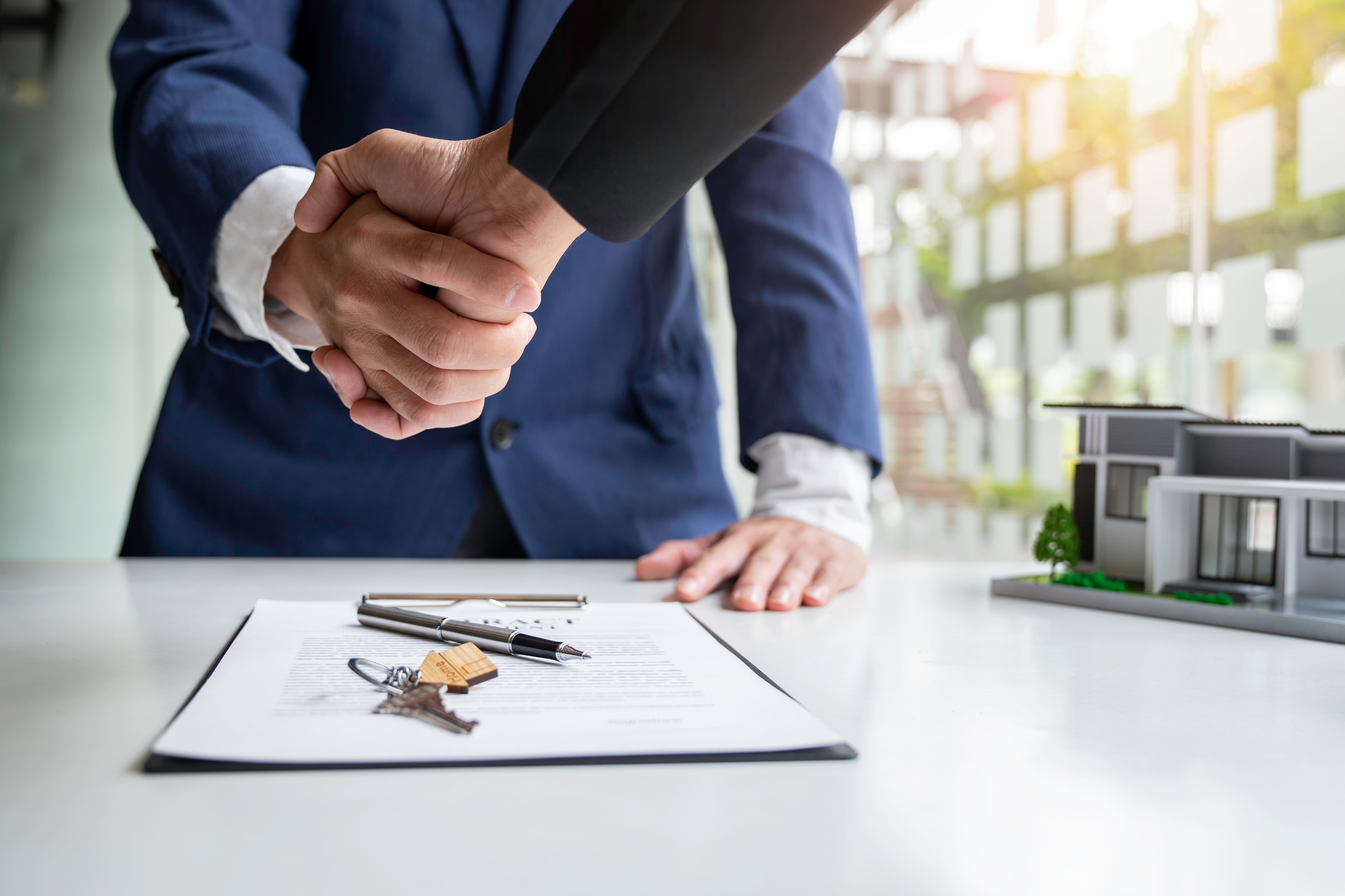 Two people shaking hands over paperwork in an office